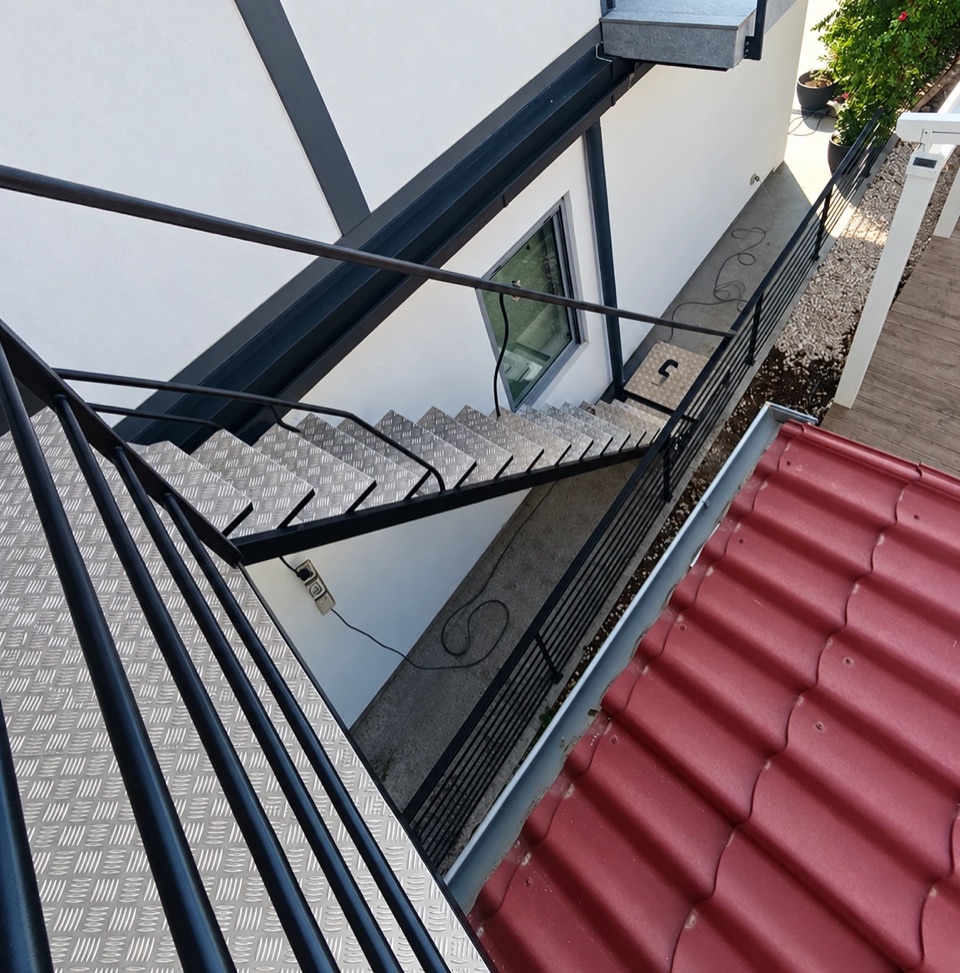 External steel staircase with chequer plate treads and a railing along the façade